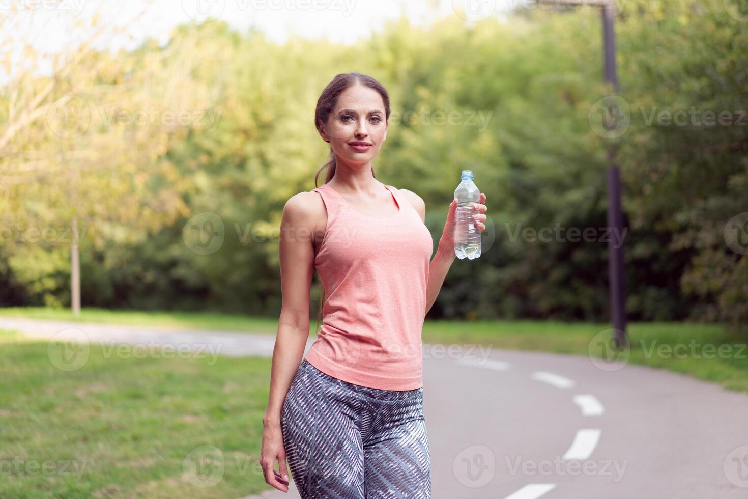 Athletic woman standing running track in summer park drink water after running exercises photo