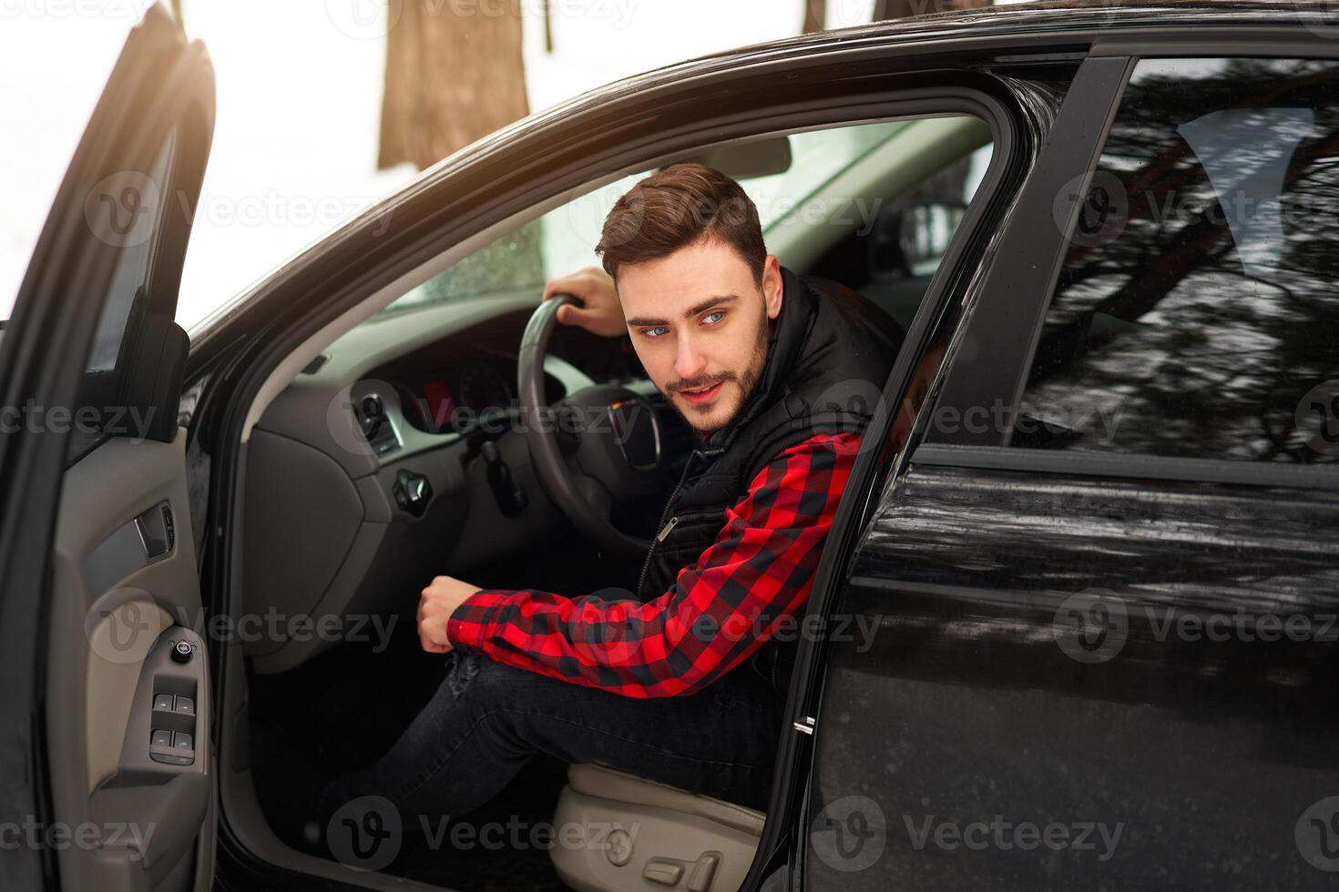 Young attractive Caucasian man sits at the wheel of his car sunny winter day. photo