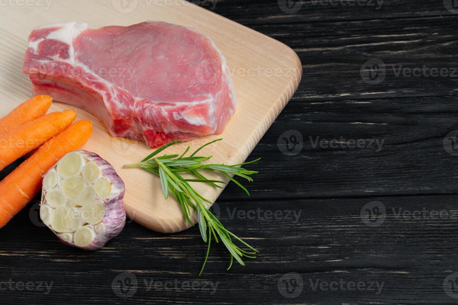 Top view of one pieces raw pork chop steaks with cherry tomatoes rosemary and garlic on a cutting board. photo