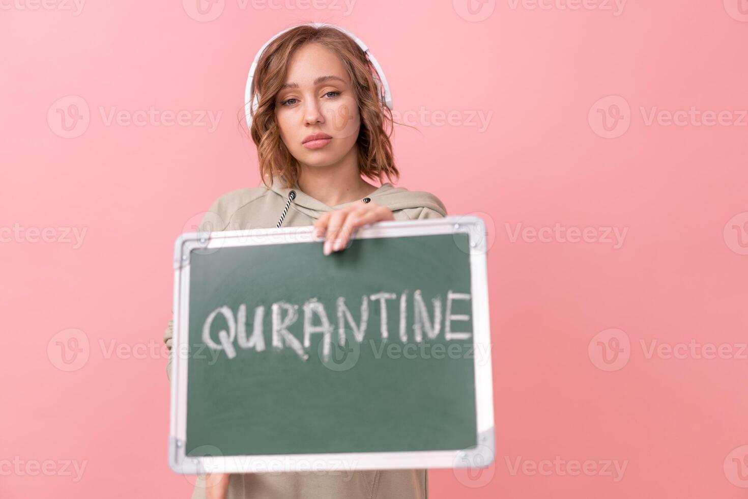 Stay home concept Woman with headphones dressed oversize hoodie holds chalkboard with the words quarantine photo