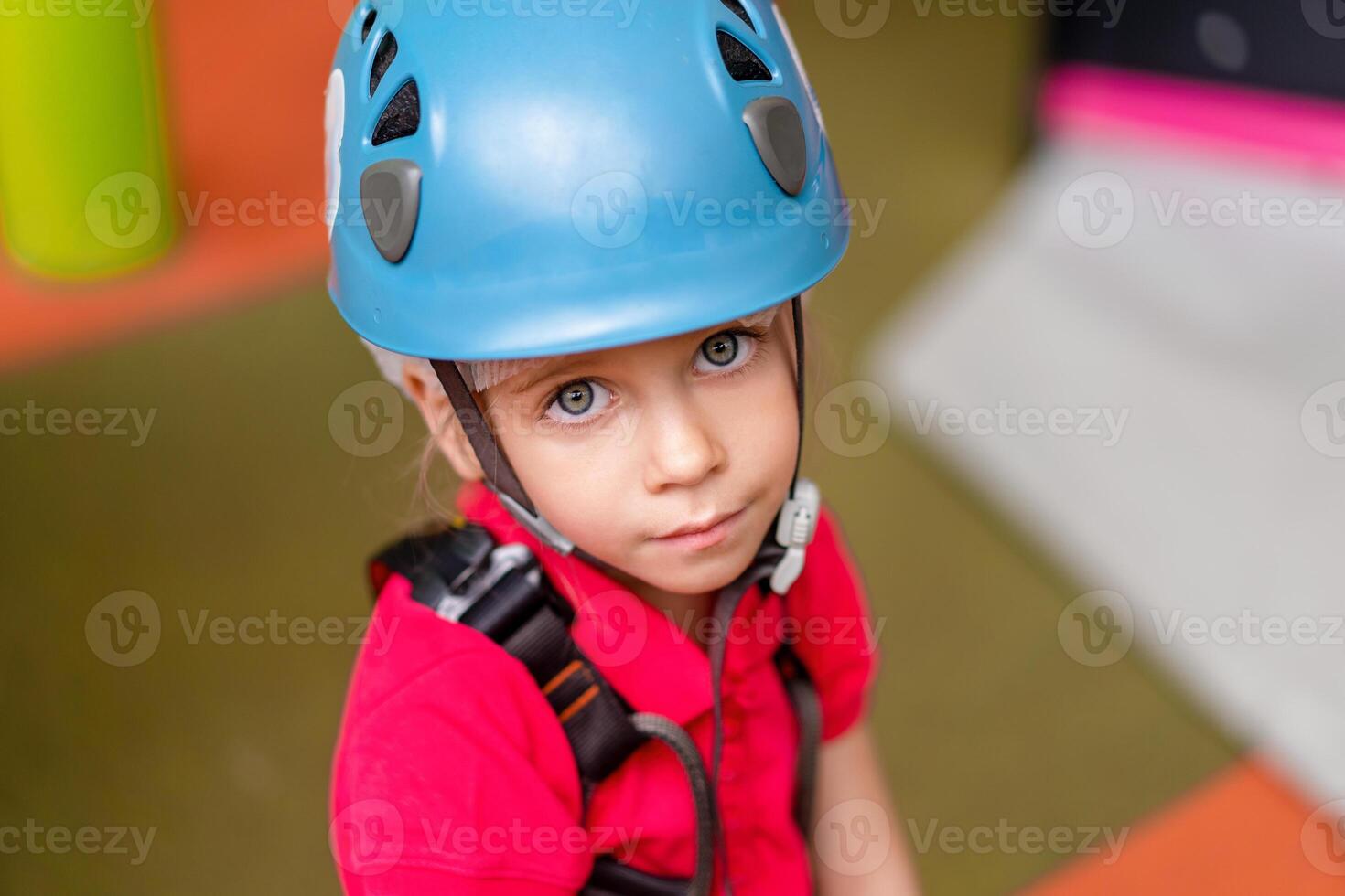 Cute little girl climber in blue protective helmet and gear for climbing standing in climber centre amusement park for children photo