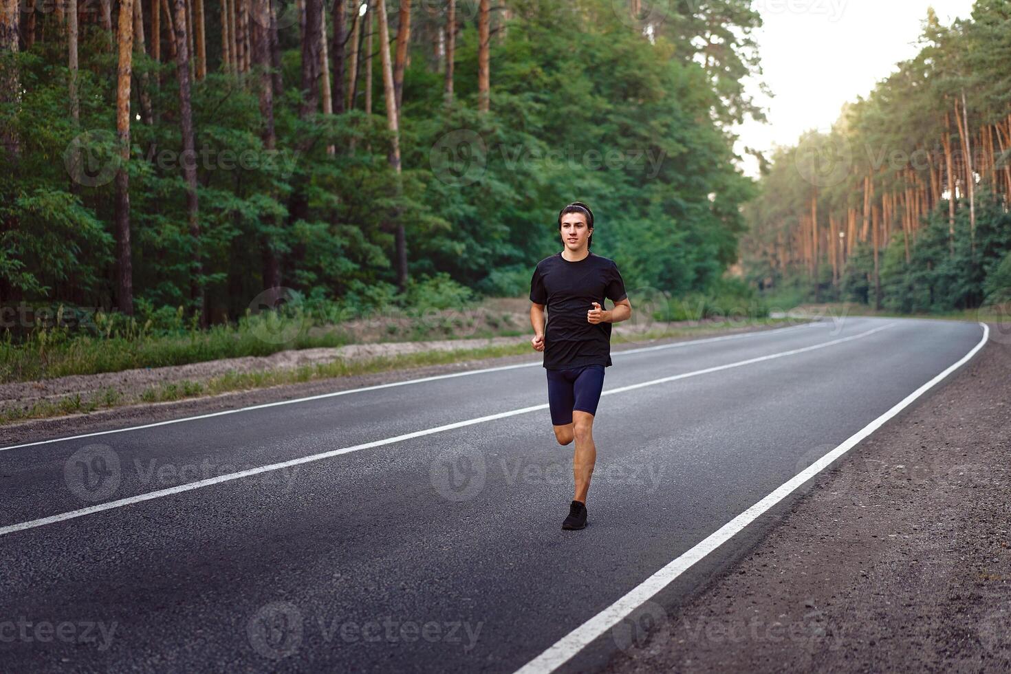 Caucasian middle age man athlete runs sunny summer day on asphalt road in the forest. photo