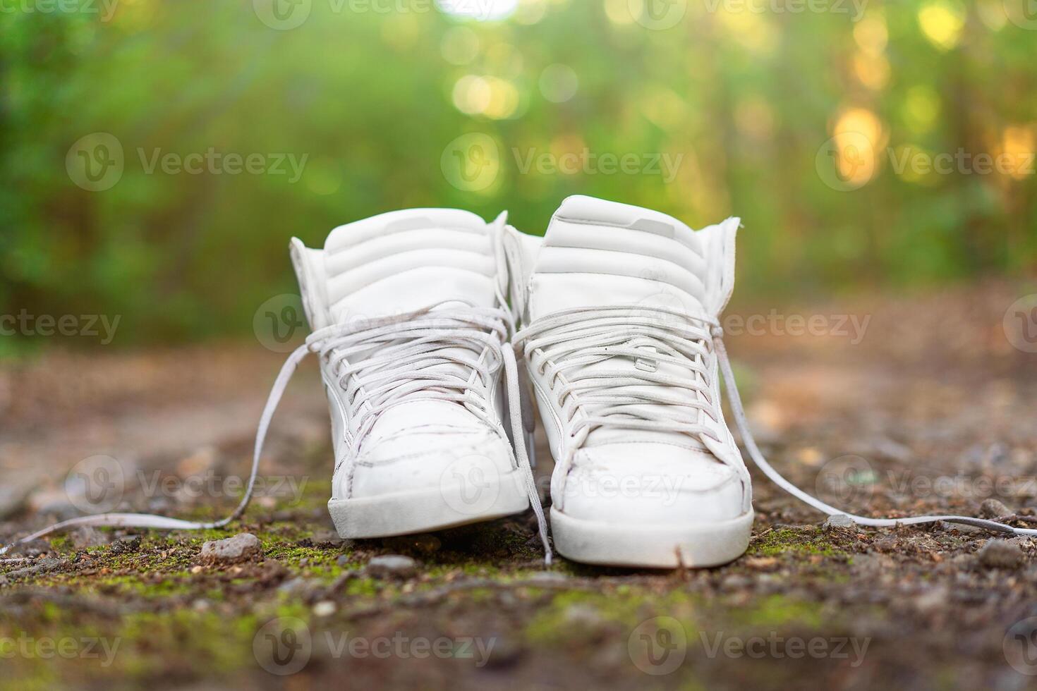 Used white high sneakers stand on a rural road that runs in the forest. photo