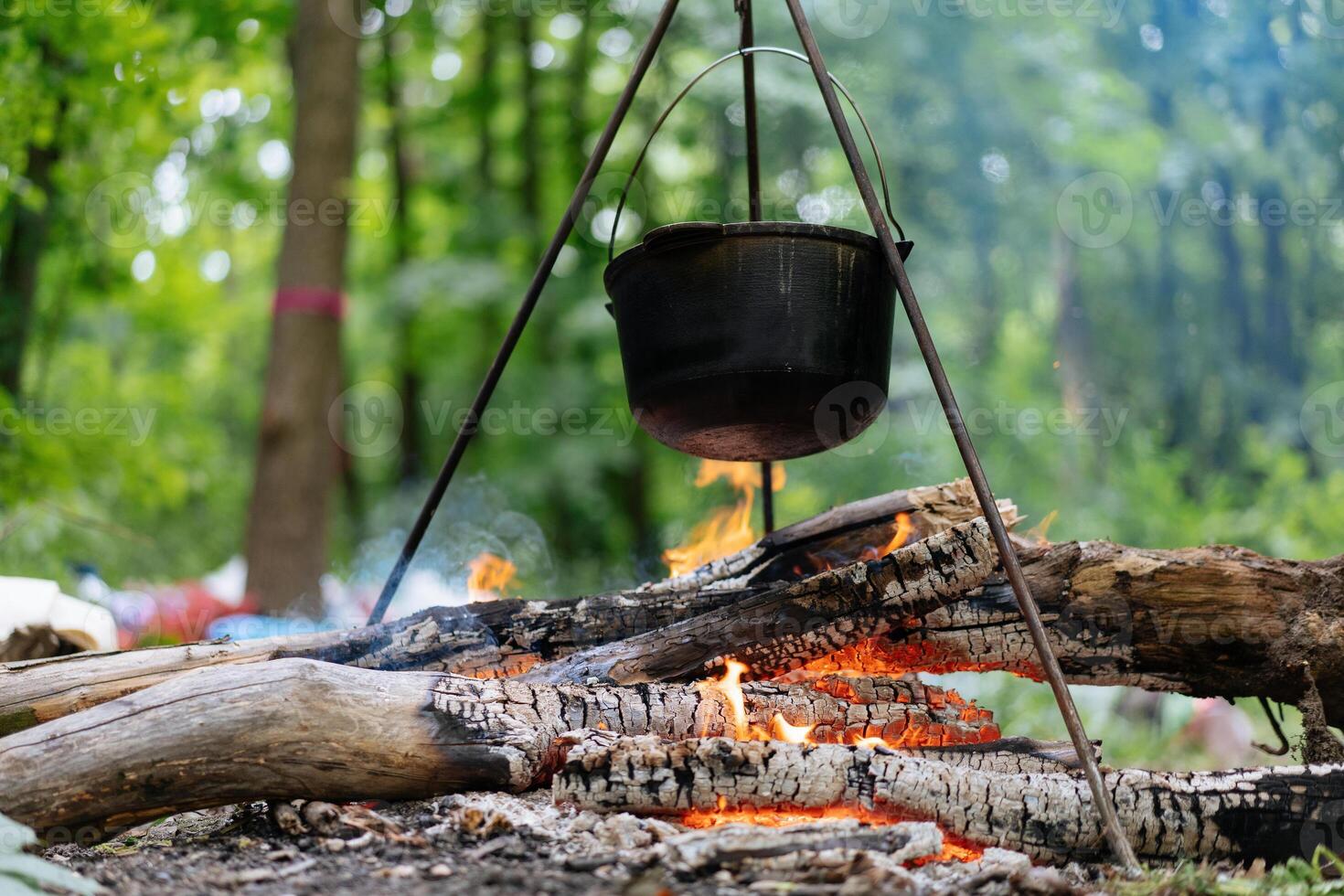 Camping outdoors. Cooking bowler hat hung on tripod over bonfire photo