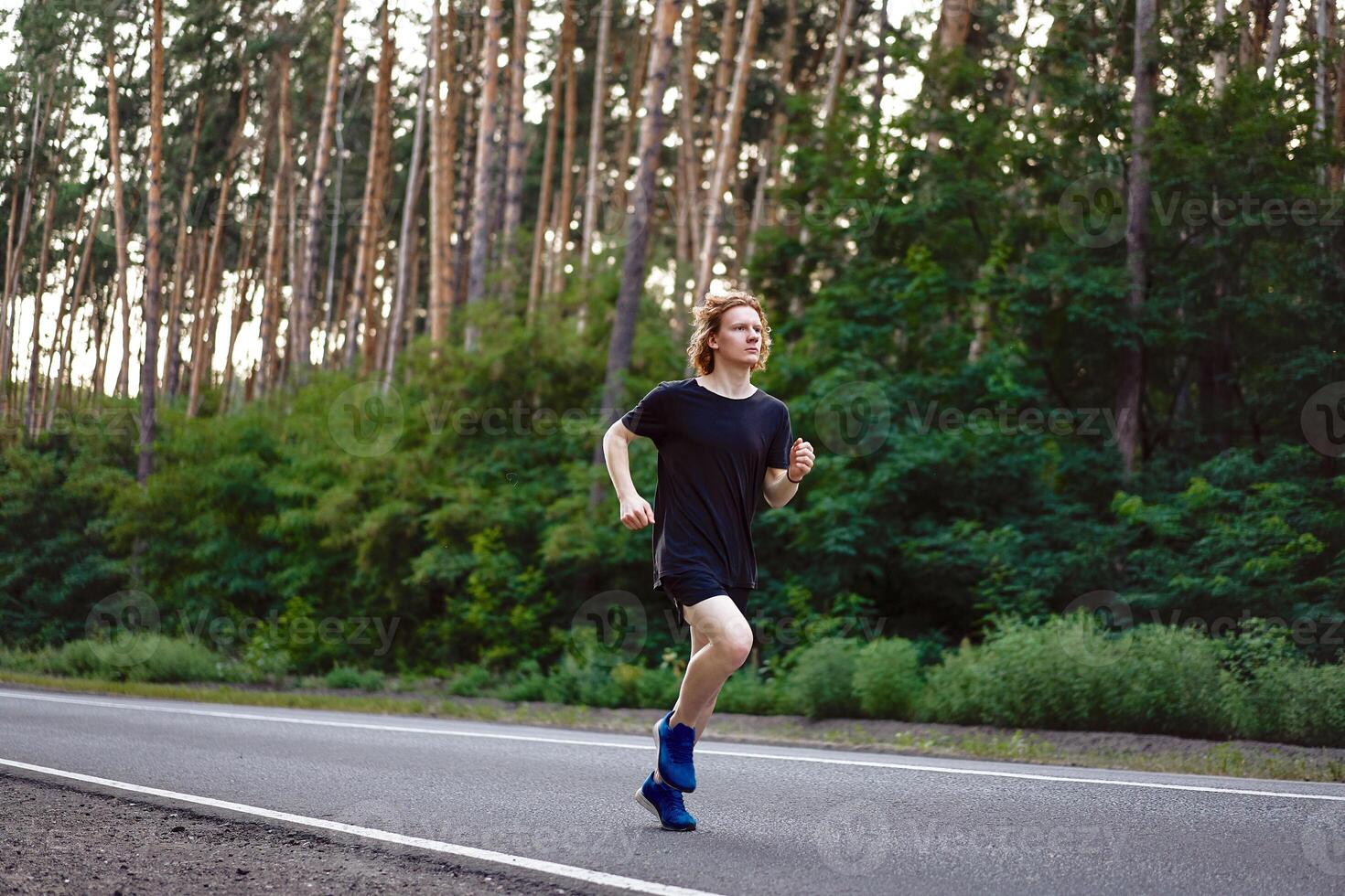 caucásico joven Rizado hombre atleta carreras soleado verano día en asfalto la carretera en el bosque. foto