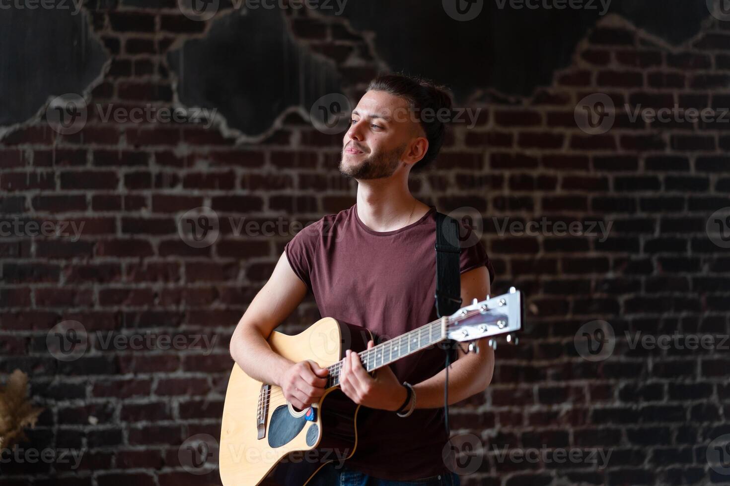 Man with acoustic guitar against brick wall playing music singing songs enjoy life Medium shoot photo