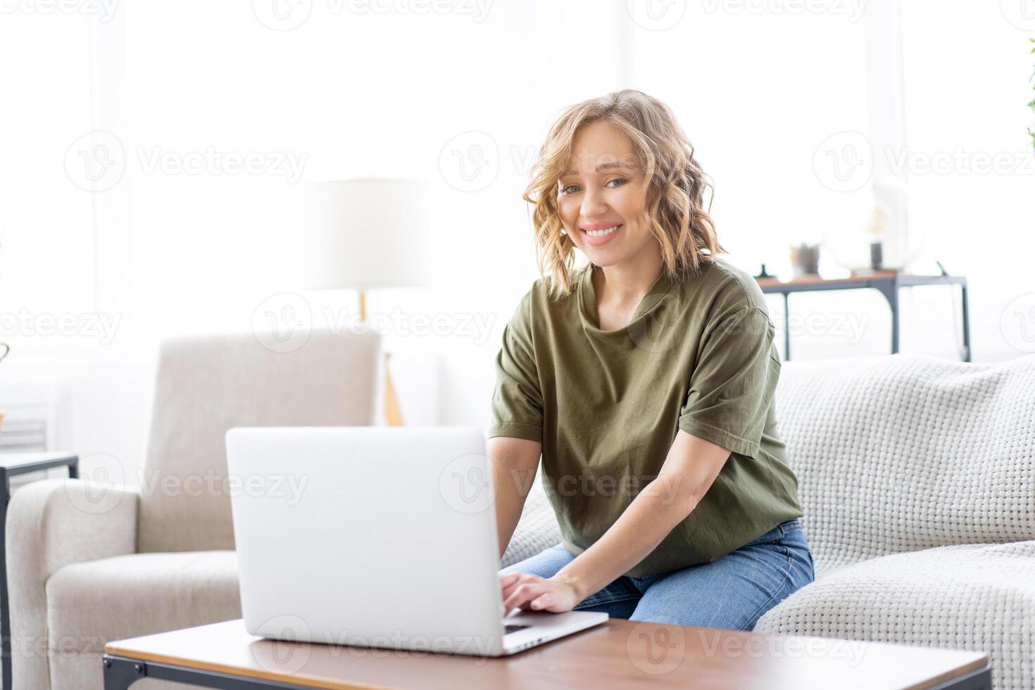 Woman using laptop computer while sitting sofa with big window on background at home interior photo