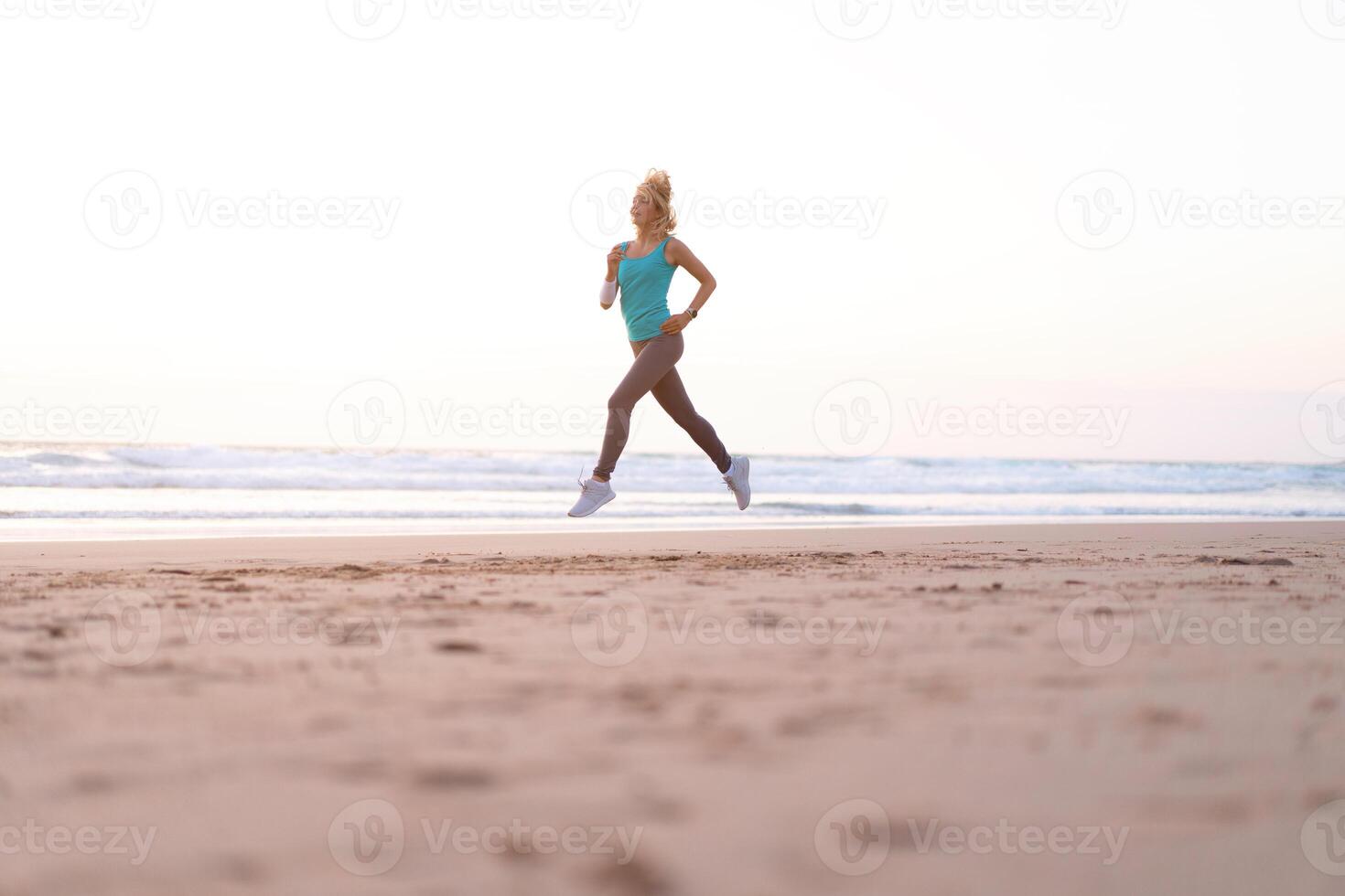 Active sporty woman run along ocean surf by water pool to keep fit and health. Sunset sand beach background with sun. Woman fitness, jogging workout and sport activity photo