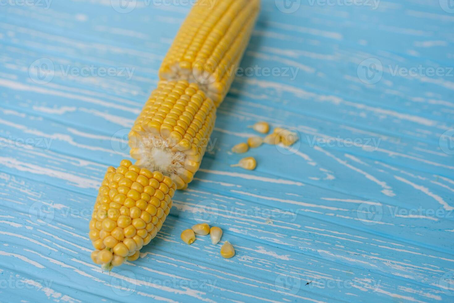 Corn cob with green leaves lies on table blue color background. photo