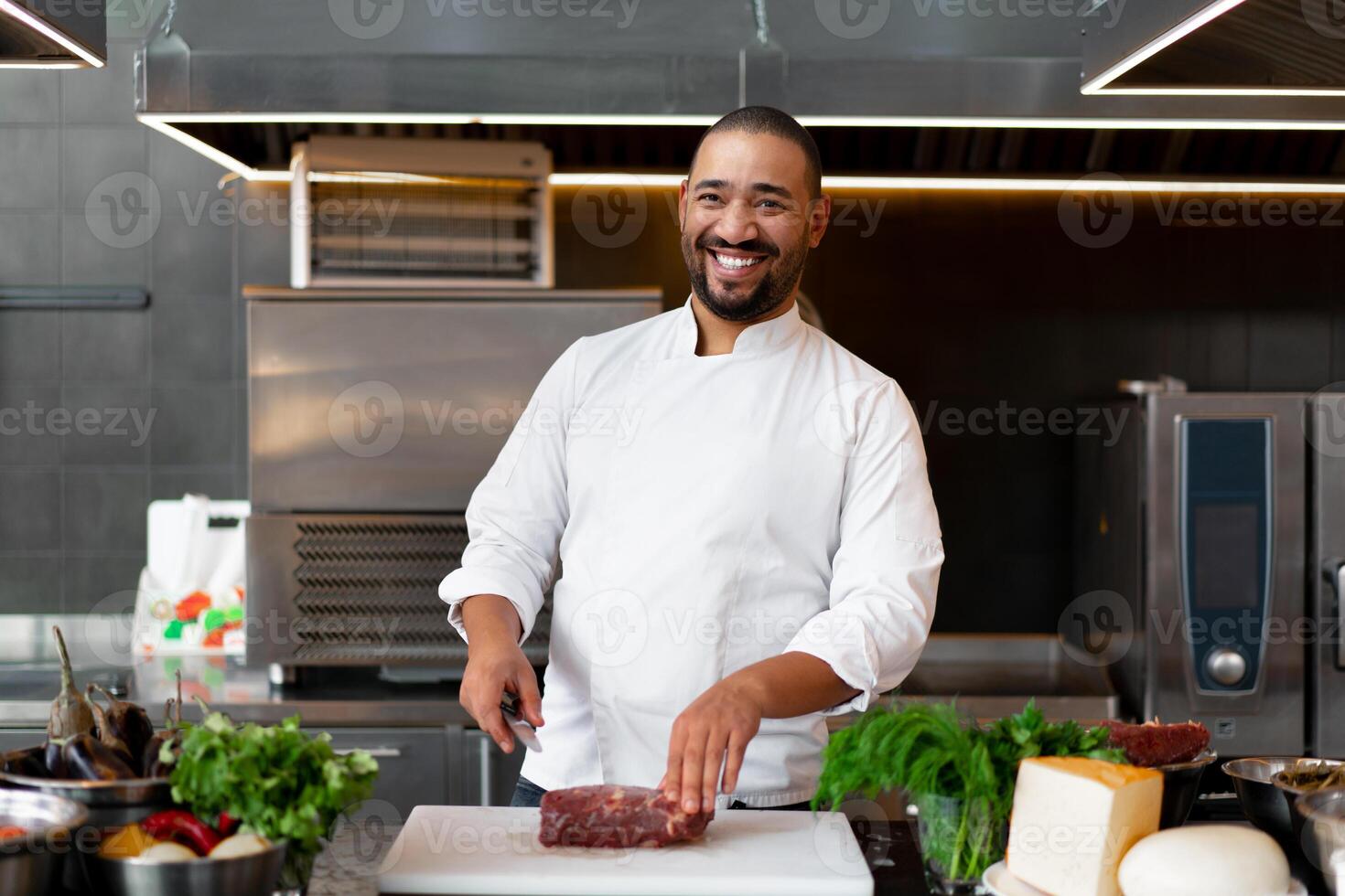 Handsome young African chef standing in professional kitchen in restaurant preparing a meal of meat and cheese vegetables. photo