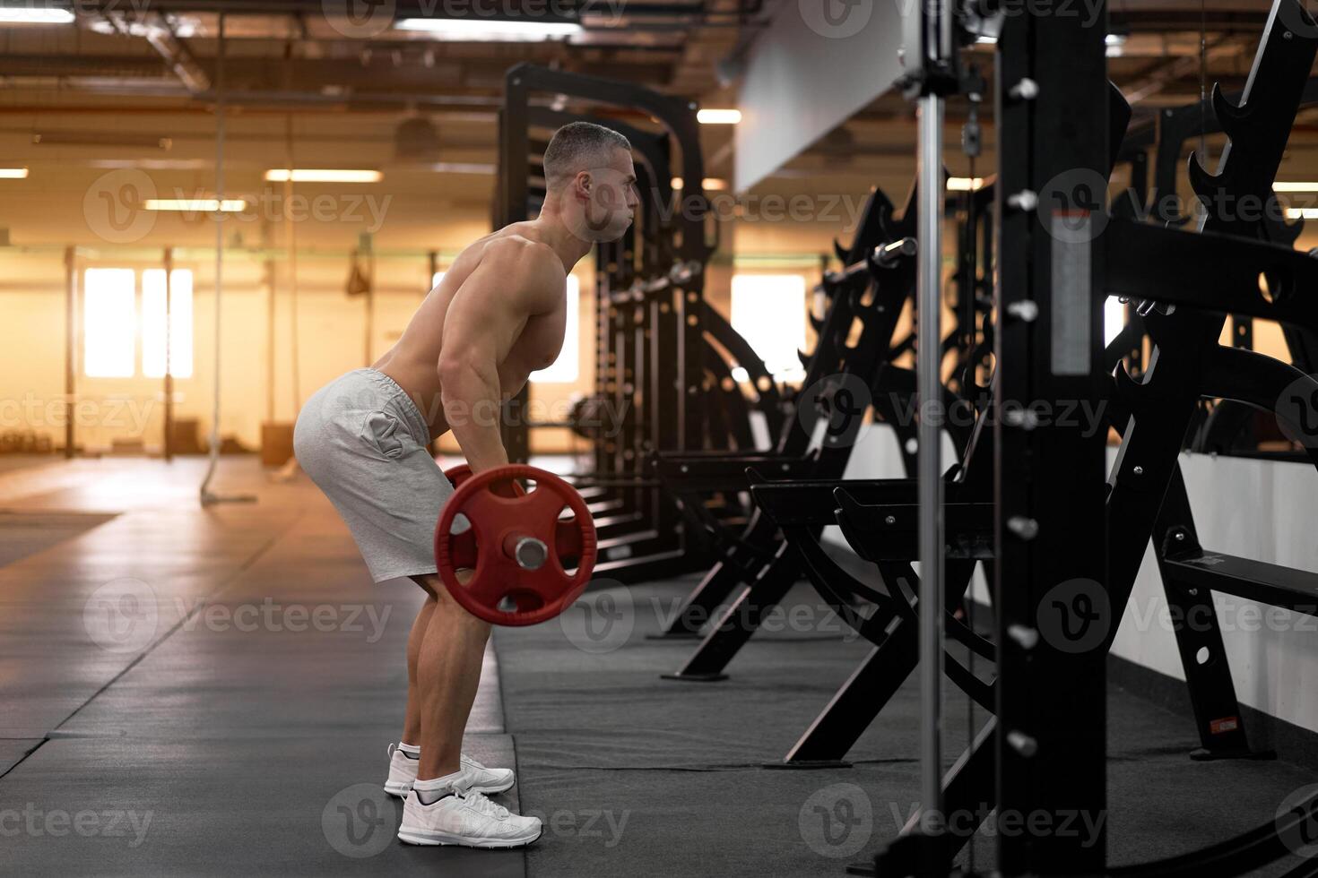 Muscular athletic bodybuilder fitness model standing in front of mirror back to camera training lift barbell indoor gym photo