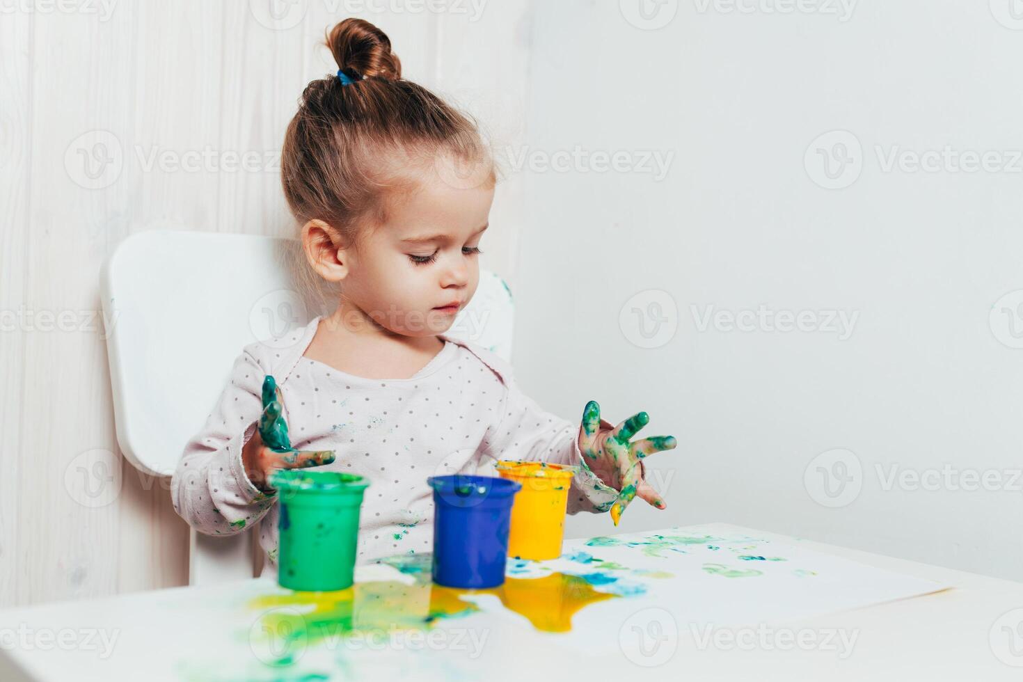 hermosa pequeño niña sorteos con dedo pinturas en un blanco sábana de papel. creativo niño desarrollo en jardín de infancia o gratis hora a hogar foto