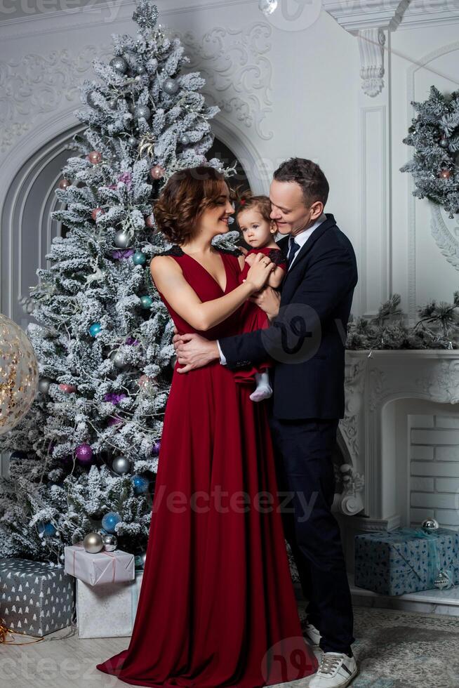 mamá papá y hija vestido en un elegante traje y elegante rojo noche vestir a un secular fiesta en honor de el nuevo año foto