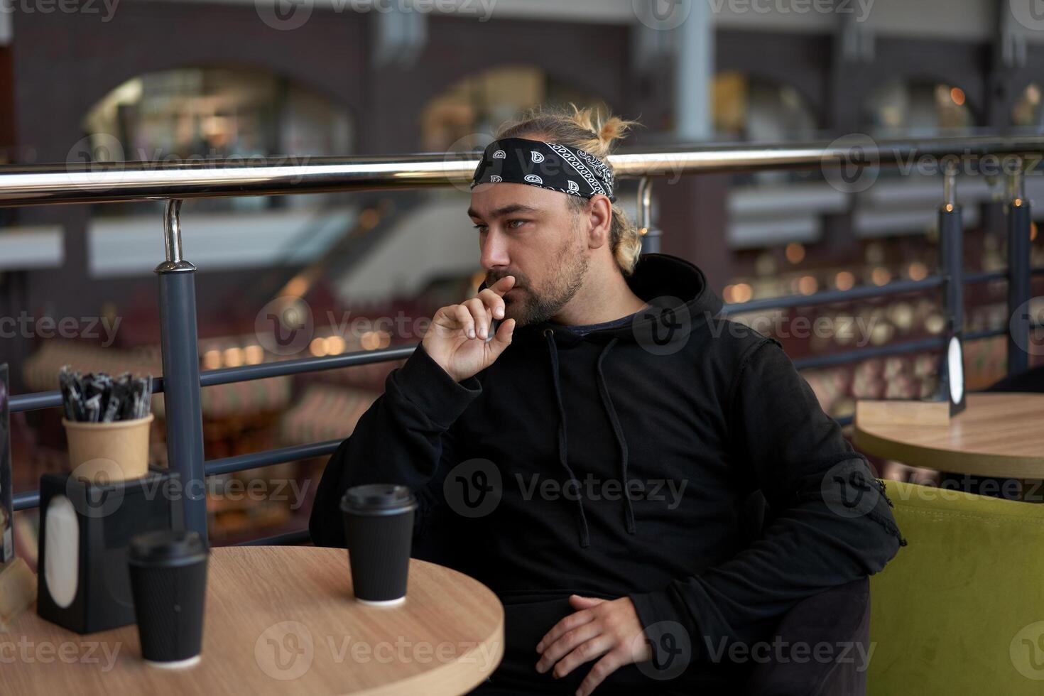 Young handsome lonely man sits cafe table sad waiting for meeting drinking coffee from a paper cup. photo
