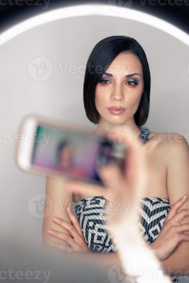 Makeup artist bsn photographs on a mobile phone the result of his work on a beautiful girl model with a ring light lamp photo