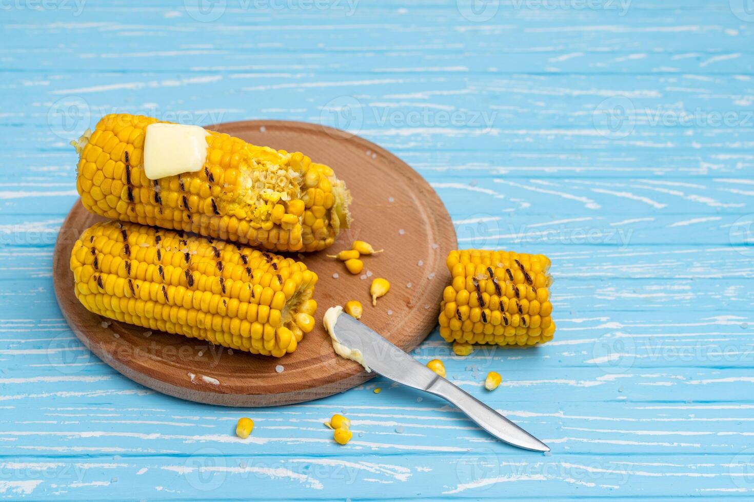 Grilled hot Corn cob lies on cutting board blue wooden table background. photo