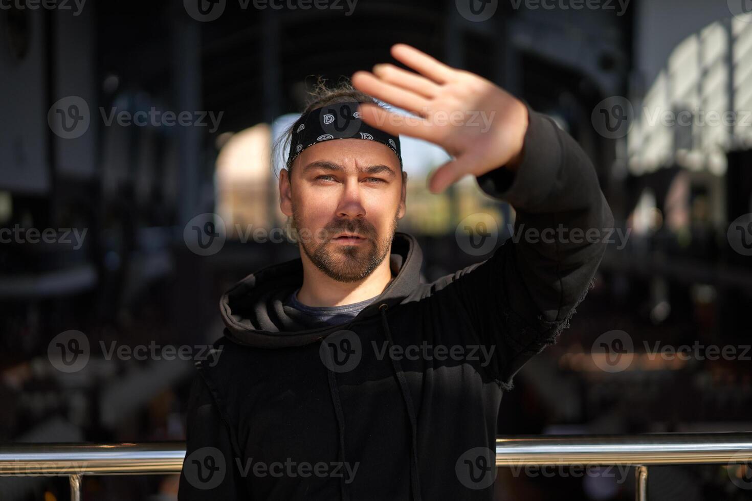 Handsome young unshaven man black hoodie and bandana stands photo