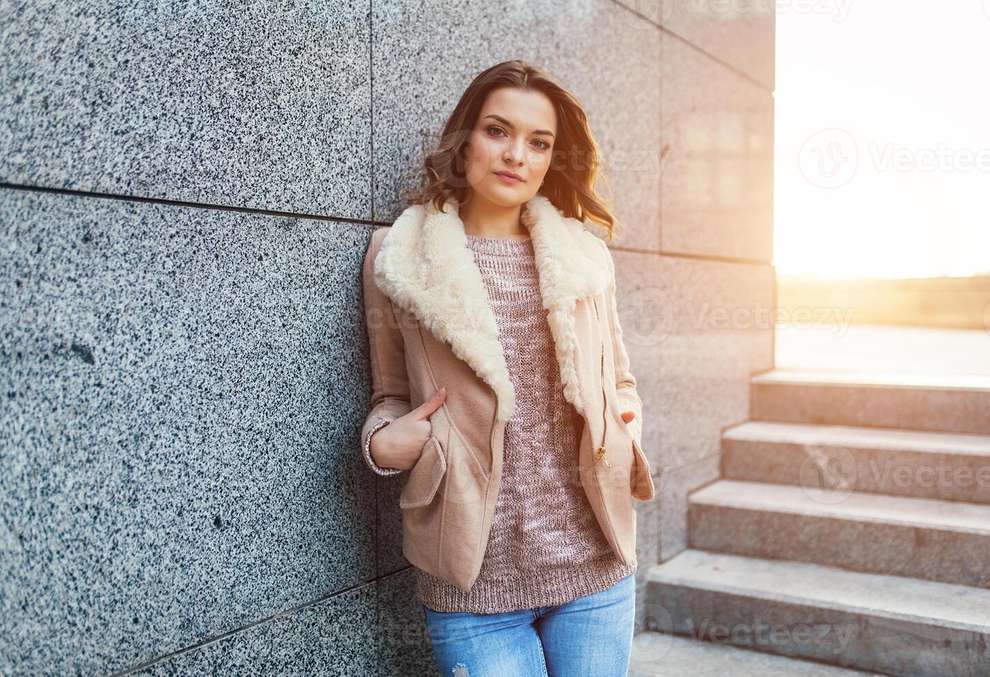 A beautiful young brunette girl walks through the autumn city in the rays of warm sunlight photo