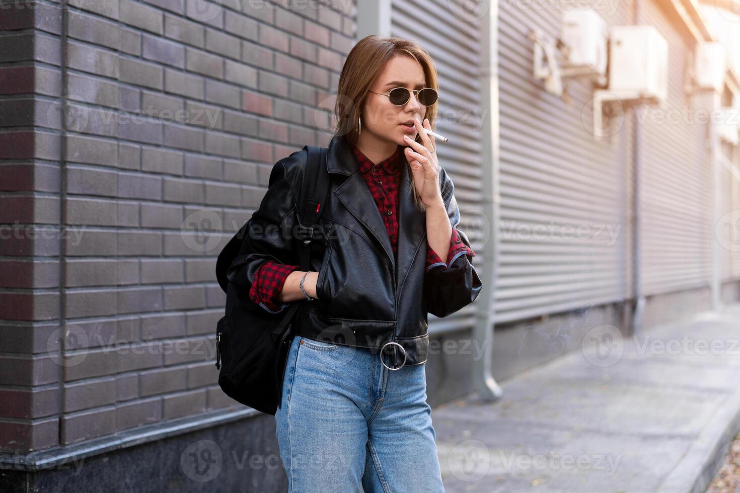 Beautiful young stylishly dressed Caucasian girl smokes cigarette on the street. photo