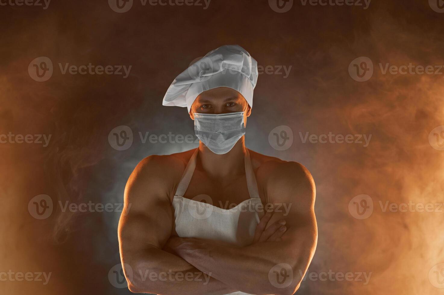 New normal concept. Muscular chef wearing protective medical mask, posing with folded arms on smoky background photo