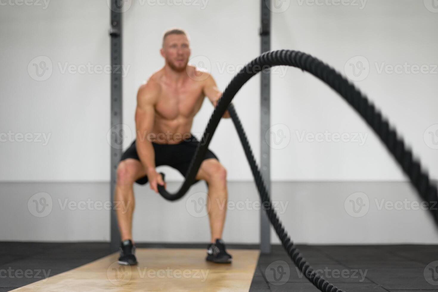 Unfocused unrecognizable man gym battle rope stamina training Athlete guy fitness exercising endurance indoor workout photo