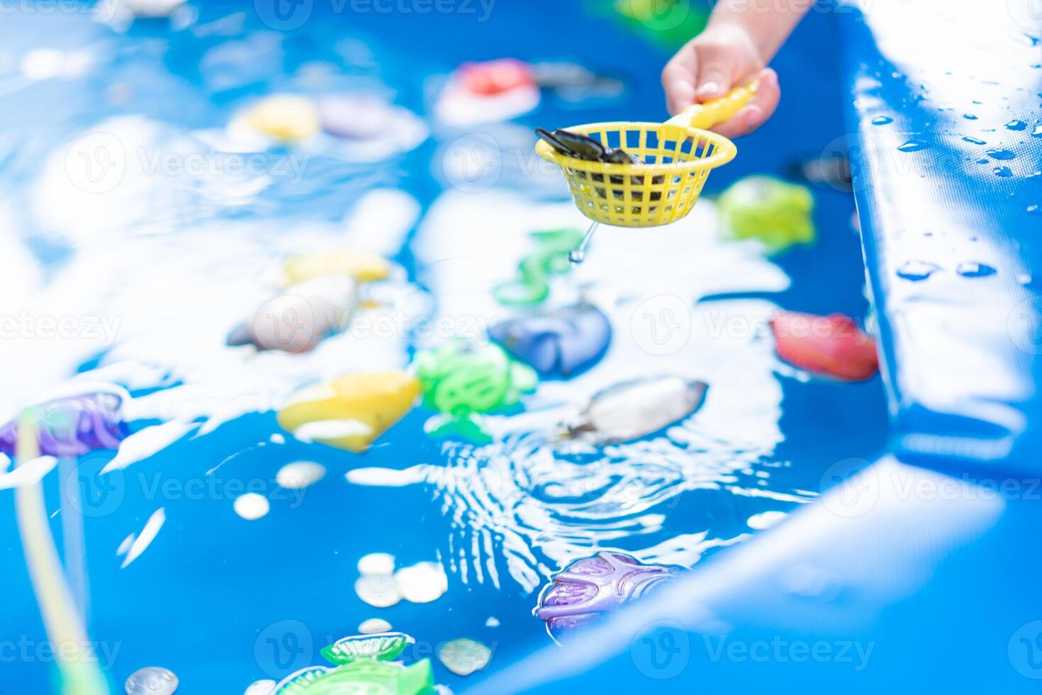 Child Fisher Catching Plastic Toy Fish On Pool Amusement Park Summer Day photo