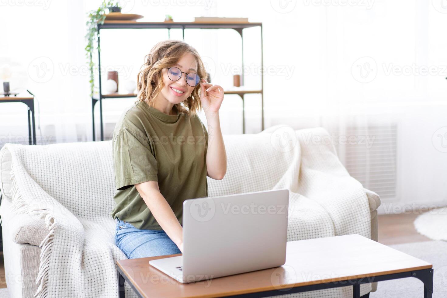 Woman glasses using laptop computer while sitting sofa with big window on background at home interior photo