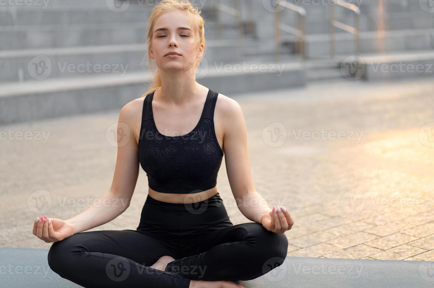 Yoga and Meditation in Modern City Caucasian Woman Relax Lotus Position Sitting Yoga Mat Outdoors Summer Park on Concrete floor photo