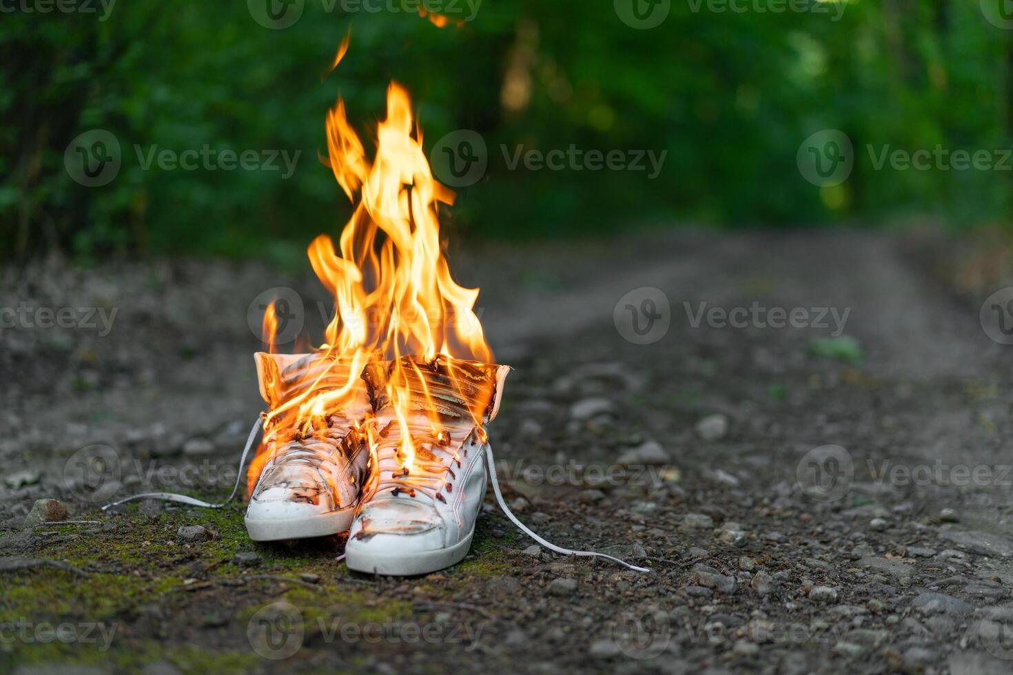 Used white high sneakers burning on a rural road that runs in the forest. photo