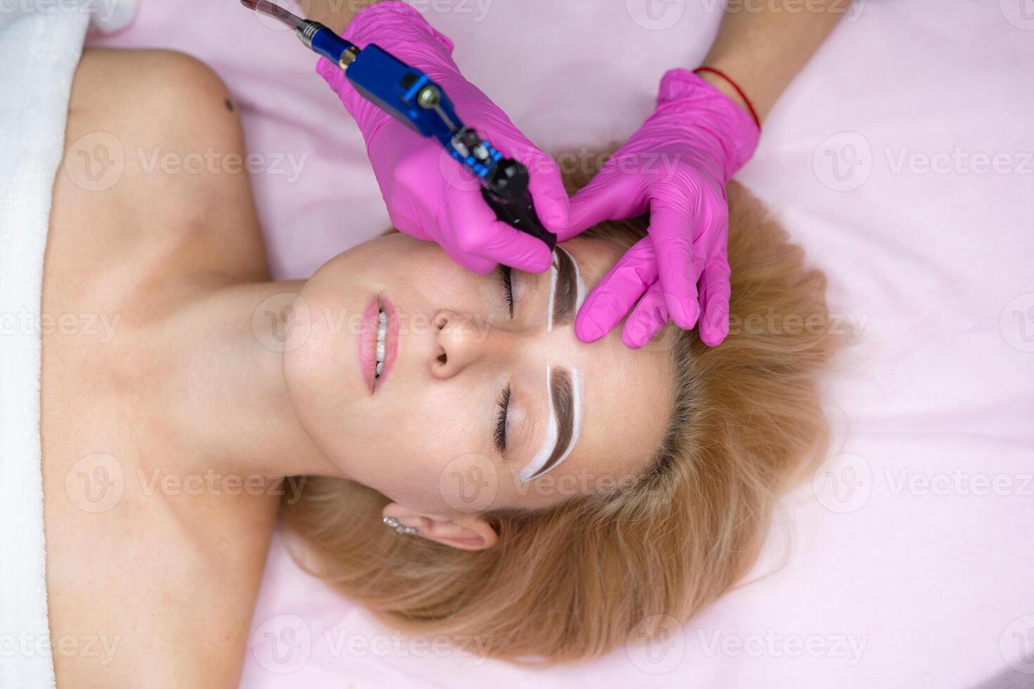 Cosmetology cabinet client lies on couch. Beautician applies marking on eyebrows. photo