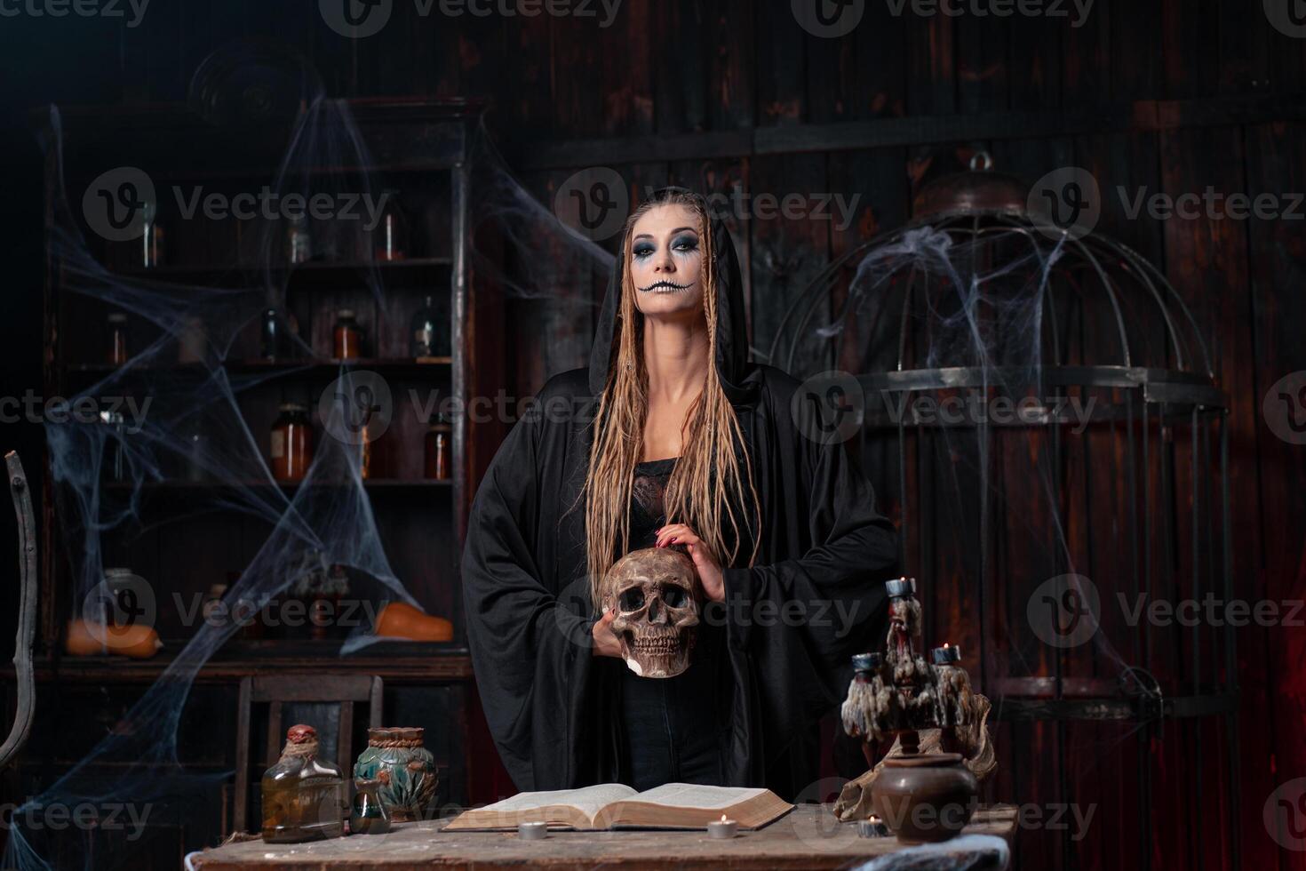 Halloween concept. Witch dressed black hood with dreadlocks standing dark dungeon room use magic book for conjuring magic spell photo