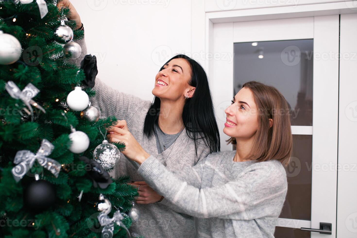 Two young women decorate the Christmas tree, preparing for the New Year's celebration photo