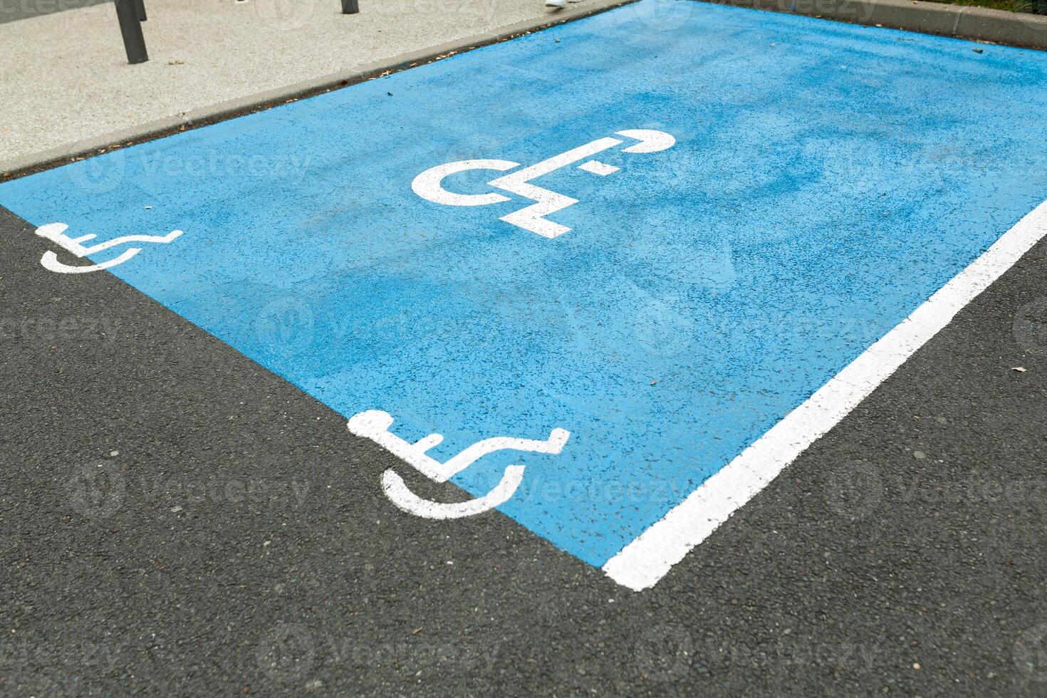 International handicapped symbol painted in bright blue on a shopping center parking space. The space is clearly marked on either side with additional white diagonal stripes. photo
