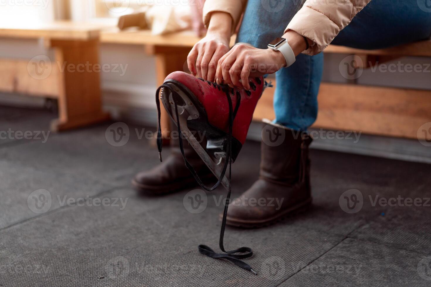 Winter time. Middle age woman put on ice skates sitting bench near ice skate rink. photo