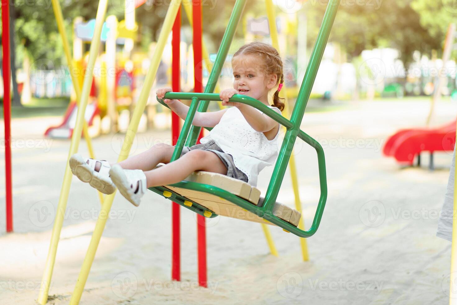 Little Caucasian girl child riding on a swing on the playground on a sunny summer day photo