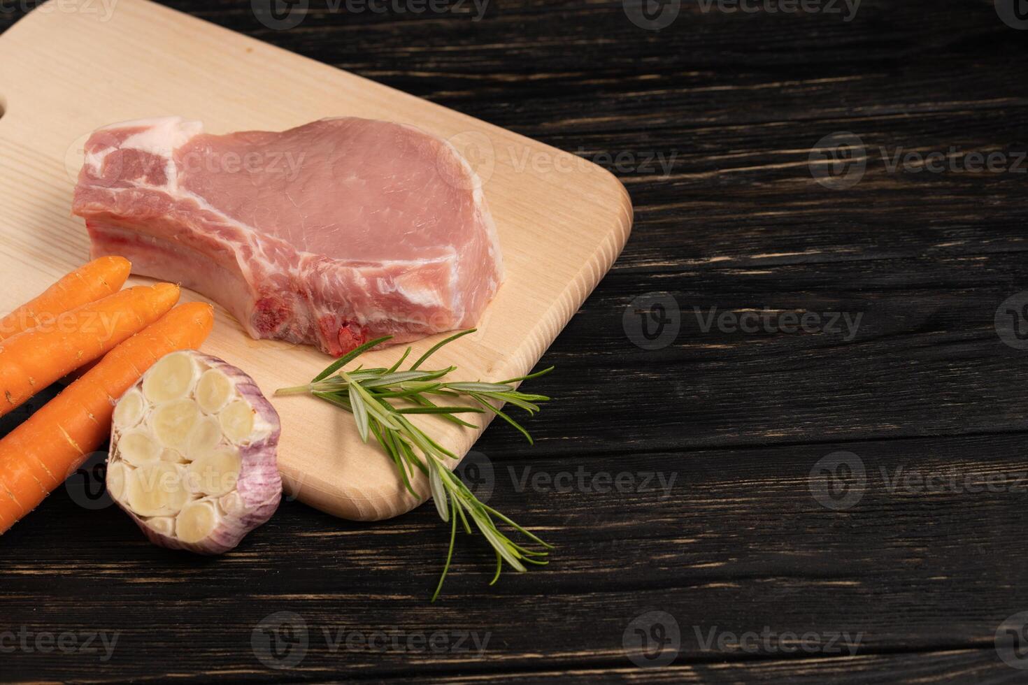 Top view of one pieces raw pork chop steaks with cherry tomatoes rosemary and garlic on a cutting board. photo