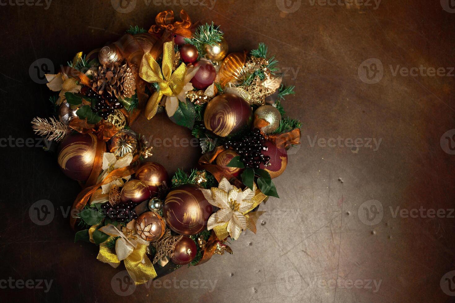 Christmas wreath on brown background with copyspace. Wreath decorated with balls and bows of gold and brown, with green leaves photo