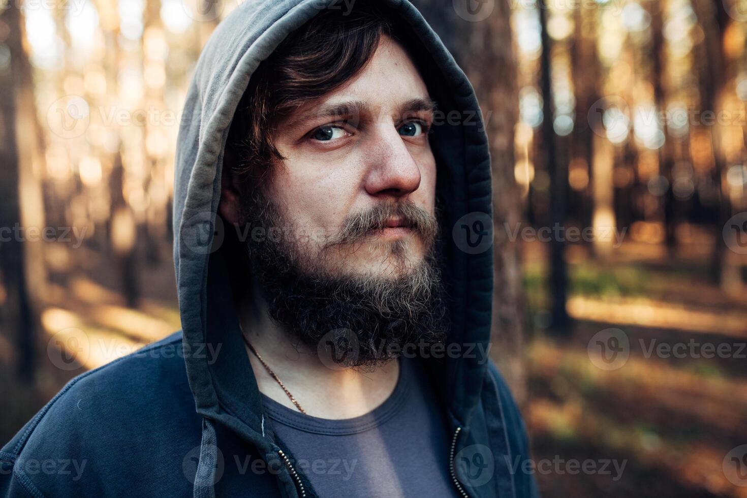 close up portrait of a bearded hipster tourist in gray hood man in the sunlight woods forest photo