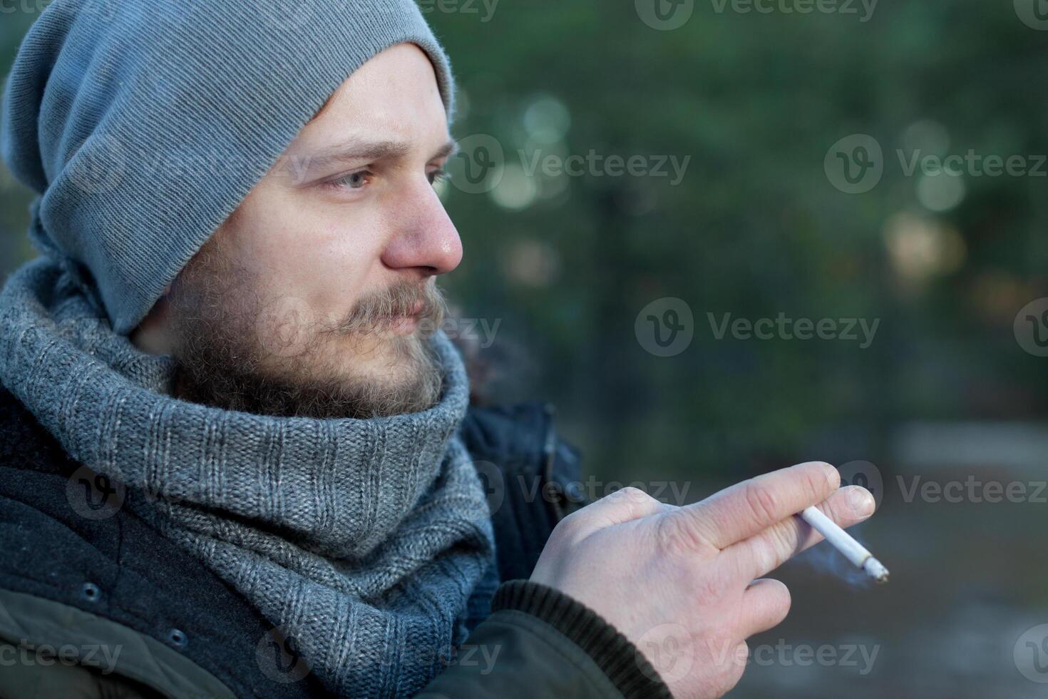 handsome sexy bearded young man hipster with long beard and mustache has stylish hair on serious hairy face smoking cigarette outdoor on green natural background photo