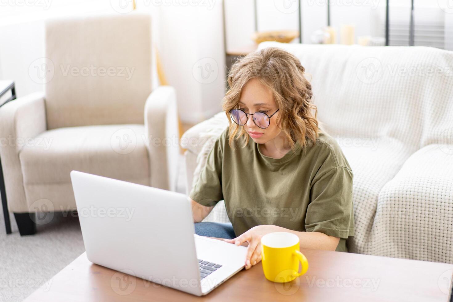 Woman glasses using laptop computer while sitting near sofa with big window on background at home interior photo