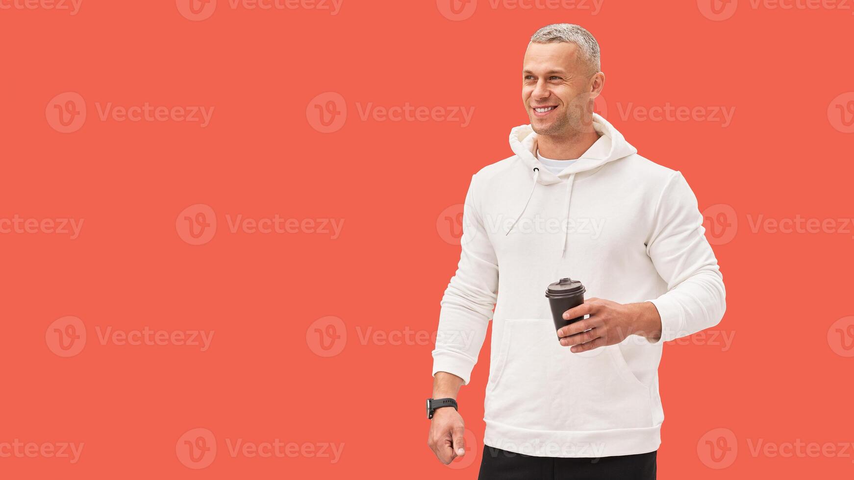 Men holding coffee in hand standing isolated red background studio shoot. Caucasian handsome male dressed white hoodie looking away positive emotions teeth smiling. photo