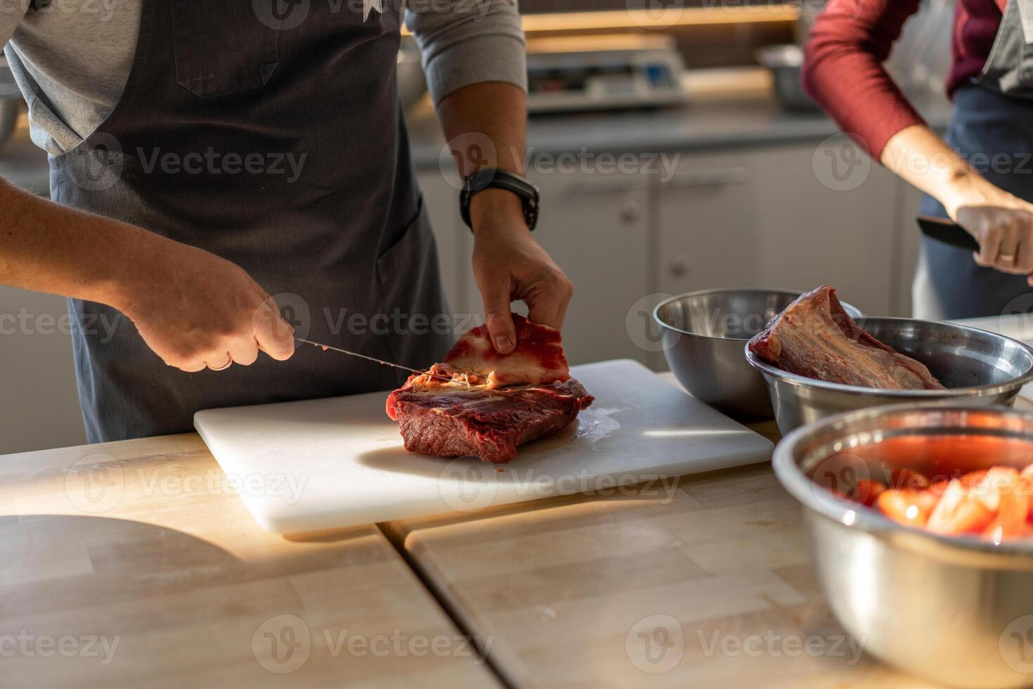 Chef in gray apron cuts meat on a plastic board. Closeup photo of the culinary process