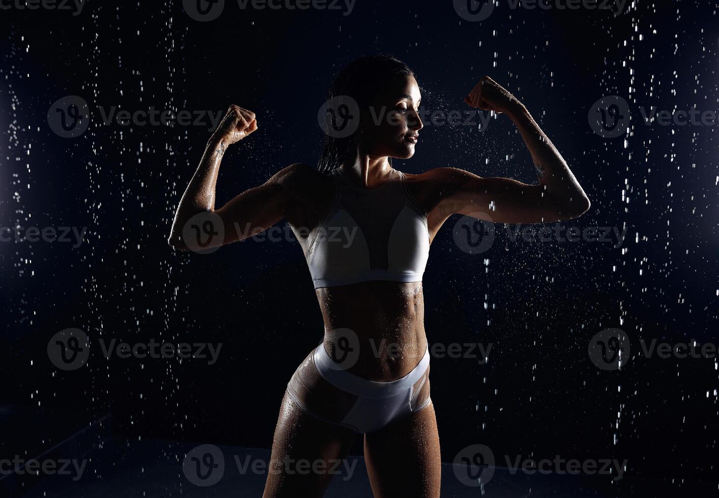 Beautiful athletic caucasian girl with a perfect figure is standing under the water. Fitness woman in a spray of water. Sports freshness. concept photo