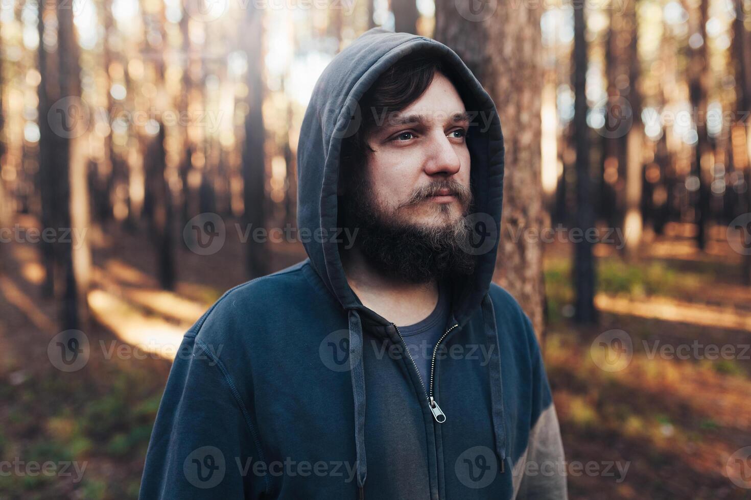 close up portrait of a bearded hipster tourist in gray hood man in the sunlight woods forest photo