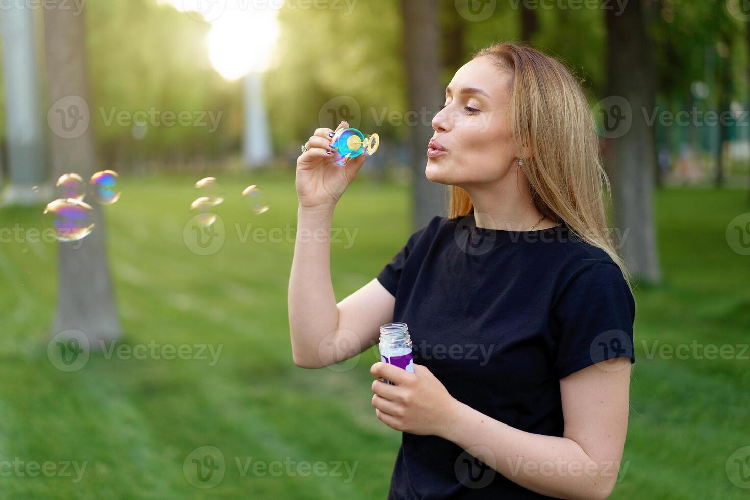 Young beautiful girl inflates soap bubbles in the summer sunny park photo