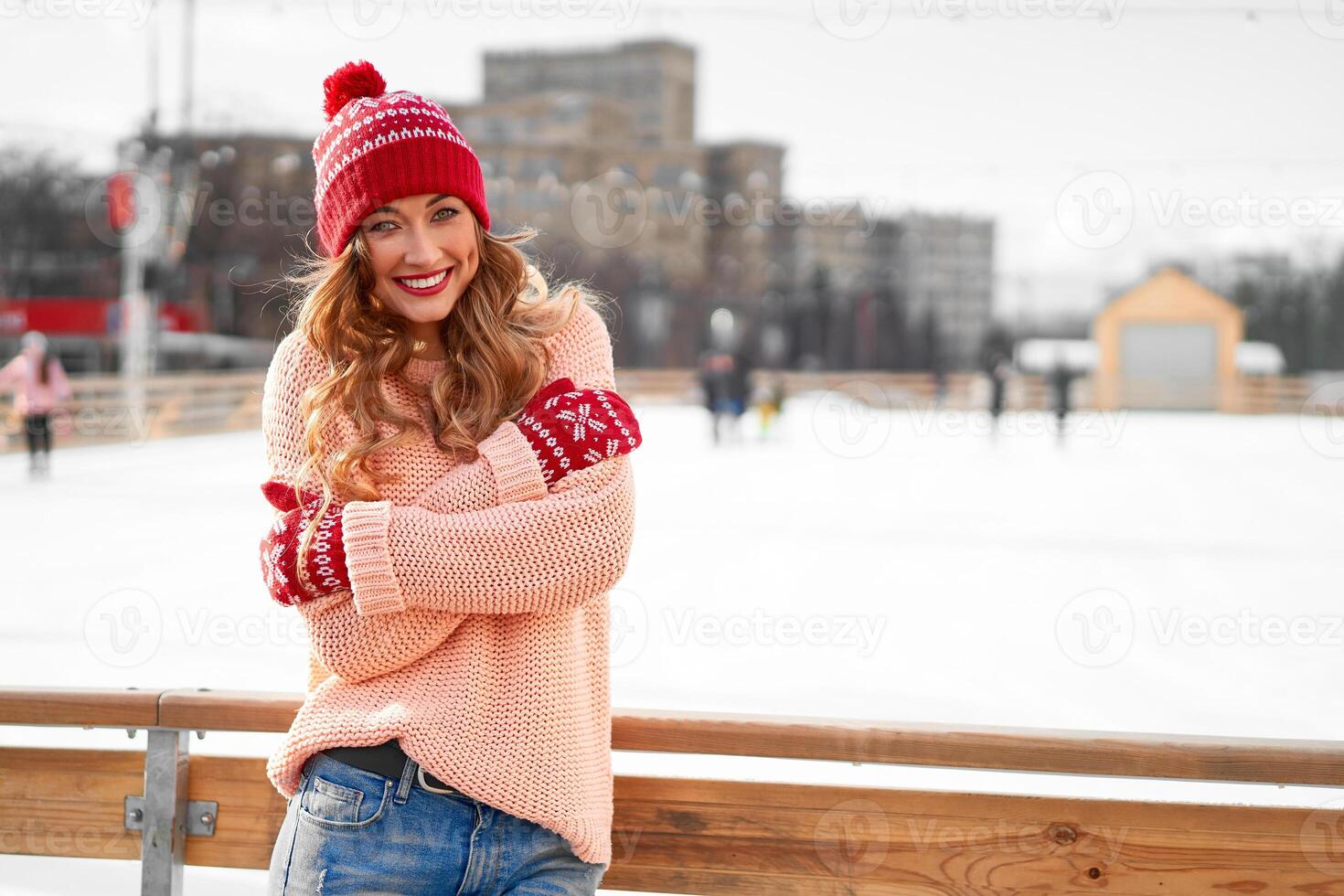 hermosa encantador de edad mediana niña con Rizado pelo calentar invierno suéter soportes hielo pista antecedentes pueblo cuadrado. foto