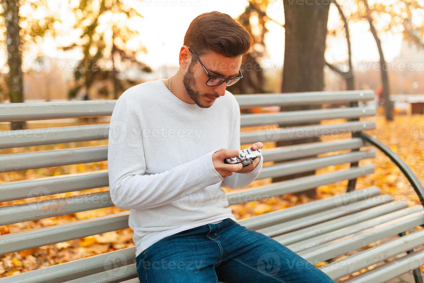 joven hermoso hipster chico camina en un hermosa otoño parque en el antecedentes de amarillo hojas en calentar soleado clima y toma imágenes en un cerdo película cámara. otoño ocio tiempo. creativo juventud foto