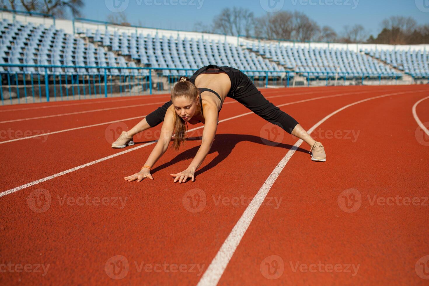 Beautiful girl in sportswear standing on the running track and preparing to run. Morning warm-up before exercise. photo