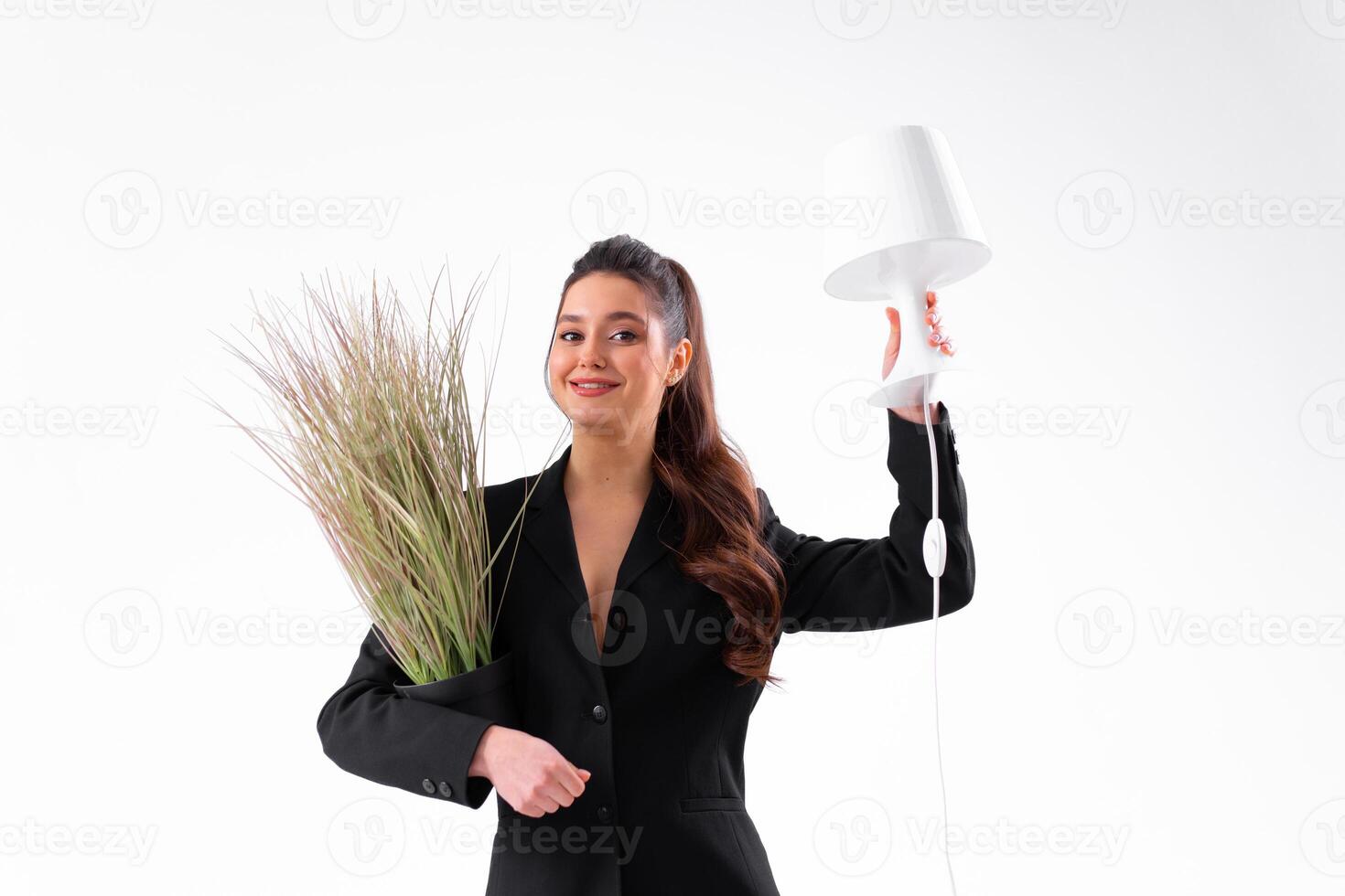 Business woman dressed black suit smile holding houseplant and lamp standing isolated on white background. Moving concept. Relocation new office with positive. photo