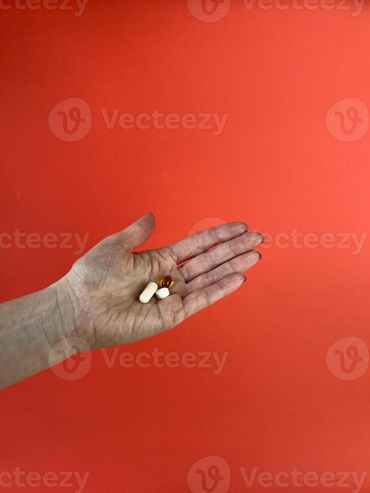 old hand holding three different pills on red background. Medicine, health and treatment concept. Ideal for medical and pharmaceutical photography photo